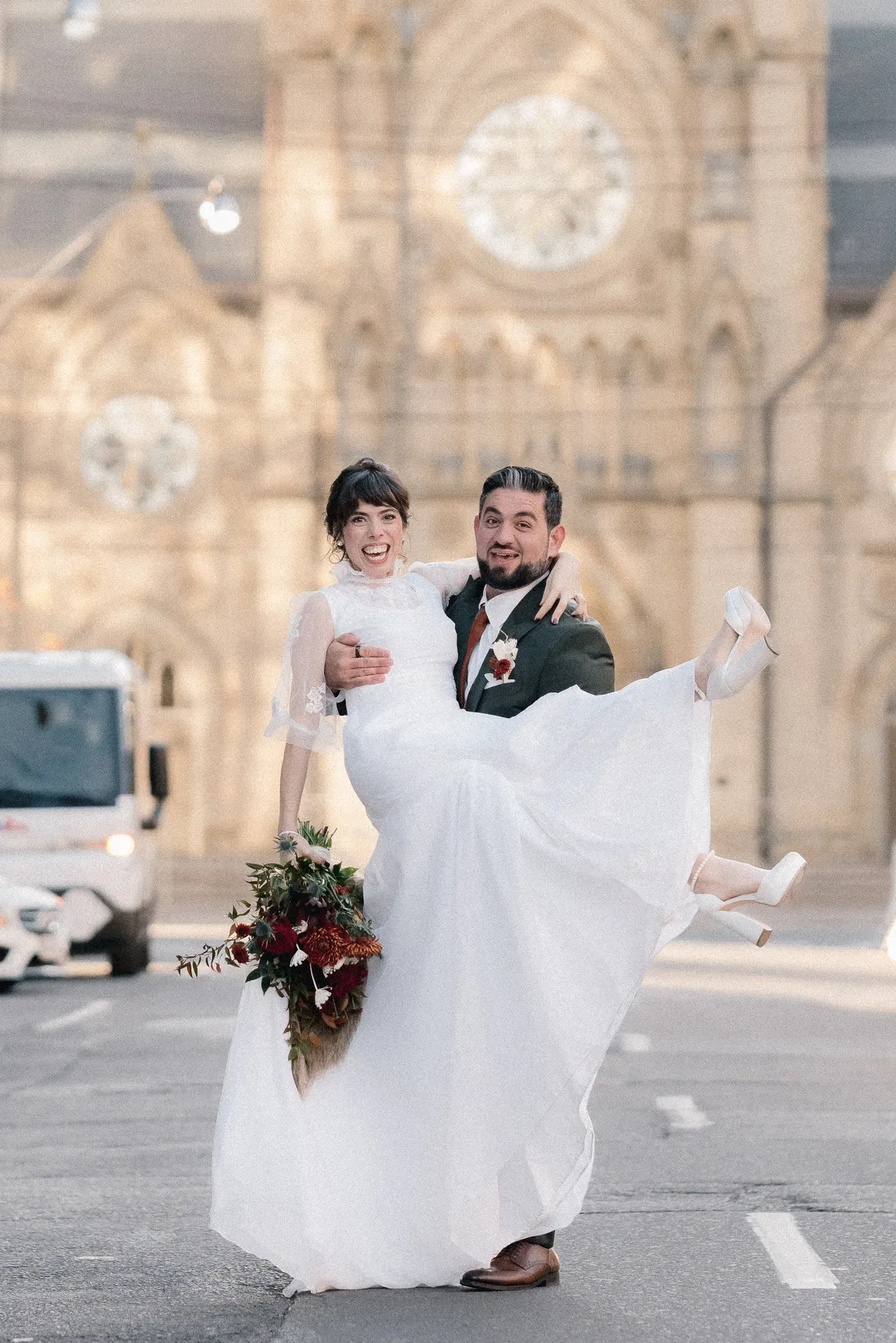 Groom carrying laughing bride in front of a Toronto cathedral